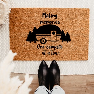 May include: A brown coir doormat with the text "Making memories One campsite at a time" and a black silhouette of a camper trailer with trees.