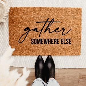 May include: A brown coir doormat with the text "gather somewhere else" in black lettering.