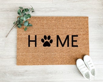 May include: A brown coir doormat with the word "HOME" in black lettering and a black paw print in the center.