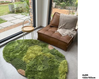 Op de afbeelding: Een groene, harige vloerkleed met een unieke, organische vorm. Het vloerkleed heeft verschillende tinten groen en bruin, waardoor een textuur en natuurlijke uitstraling ontstaat. Het vloerkleed meet 122 cm x 183 cm.