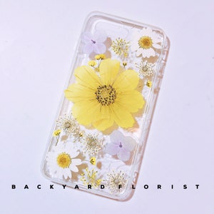Peut inclure: Une coque de t&eacute;l&eacute;phone transparente avec des fleurs press&eacute;es. Les fleurs sont jaunes, blanches et violettes. La coque a un dos et des c&ocirc;t&eacute;s transparents.
