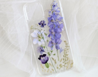 May include: A clear phone case with pressed purple and white flowers. The flowers are arranged in a bouquet-like design.
