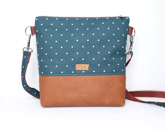 Può includere: Una borsa a tracolla rettangolare con una sezione superiore in tessuto color verde ottanio a pois bianchi e una base marrone tinta unita. La borsa presenta un'etichetta del marchio in similpelle marrone, una cerniera superiore e una tracolla.