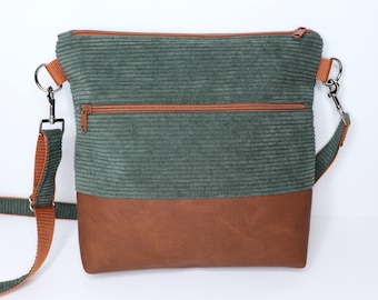 Può includere: Una borsa a tracolla con una sezione superiore in velluto a coste verde scuro e una base marrone liscia. La borsa include una tasca orizzontale con cerniera sul davanti, una chiusura superiore con cerniera e una tracolla regolabile arancione.
