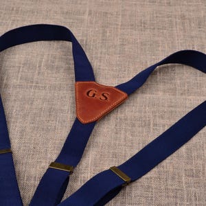 Puede incluir: Tirantes azul marino con un parche de cuero marrón con las iniciales "G.S.". Los tirantes tienen ajustadores de metal color latón y están hechos de un material tejido resistente. El diseño es clásico y adecuado para varios atuendos.