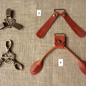 May include: An assortment of hardware components, including metal clips and leather straps. The metal pieces have a bronze finish, while the leather straps are a reddish-brown color. The items are arranged on a textured, neutral-toned surface.