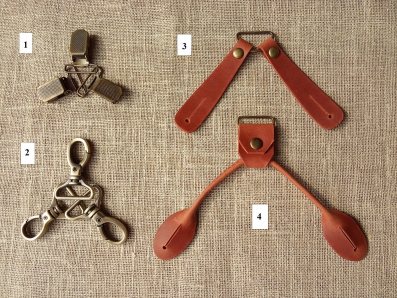May include: An assortment of hardware components, including metal clips and leather straps. The metal pieces have a bronze finish, while the leather straps are a reddish-brown color. The items are arranged on a textured, neutral-toned surface.