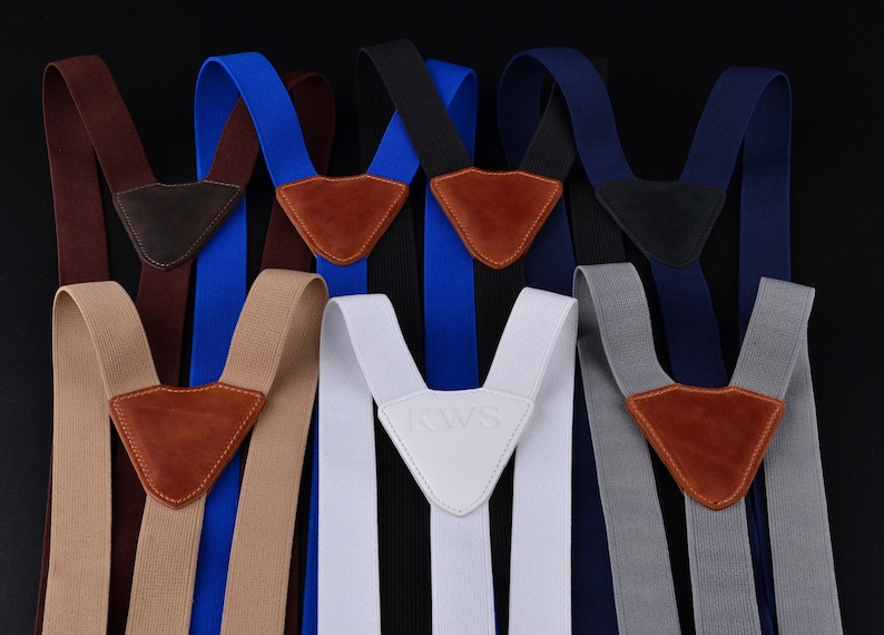 May include: Assortment of suspenders in various colors, including brown, blue, black, navy, white, and gray. Each pair features a leather or leather-like patch at the Y-back and adjustable straps. The white pair has "RAWS" embossed.