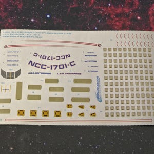 May include: A white decal sheet with a Star Trek USS Enterprise NCC-1701-C model kit decal set. The sheet includes the ship's registration number, name, and various other details.