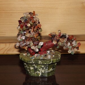 Può includere: Un bonsai decorativo fatto di pietre preziose colorate e filo di rame. L'albero ha un tronco e rami rossi, con pietre verdi, rosse e trasparenti. È in un vaso verde ottagonale, di circa 10 cm di diametro.