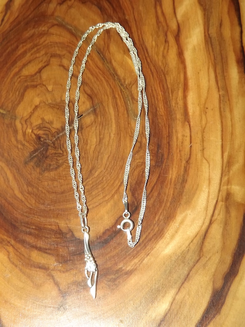 Peut inclure: Un collier en argent avec un pendentif en argent en forme de fleur stylis&eacute;e.
