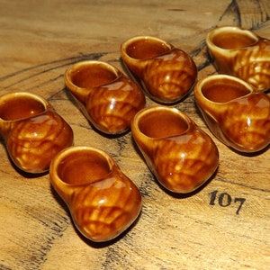 Peut inclure: Sept petits sabots en céramique brune, chacun avec un motif de glaçure unique, sont disposés sur une surface en bois. Les sabots sont tous de taille et de forme similaires, et ils ont une pointe arrondie et un petit talon.