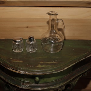 Peut inclure: Trois bouteilles en verre sur une surface en bois vert. Deux des bouteilles sont petites et ont des couvercles argentés. La plus grande bouteille est transparente et porte l'inscription "Puget".