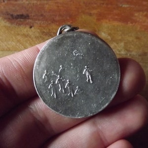 May include: Silver pendant with a design of stick figures running around a circle.