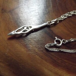 Peut inclure: Un collier en argent avec un pendentif d&eacute;licat et complexe. Le pendentif est en forme d'oiseau stylis&eacute; avec un motif circulaire au centre. La cha&icirc;ne est de style corde torsad&eacute;e.