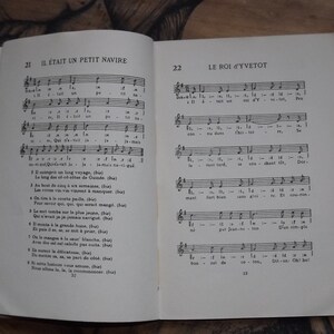 May include: A vintage book with a black and white cover featuring musical notes and lyrics for the French songs "Il &eacute;tait un petit navire" and "Le Roi d'Yvetot".