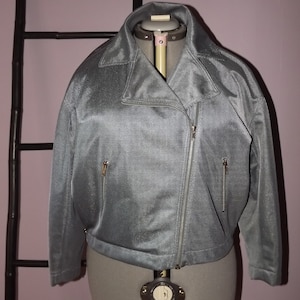 Op de afbeelding: Een grijs, geritst jack met een opstaande kraag. Het jack is gemaakt van een textuurstof en heeft een licht ingekorte lengte.