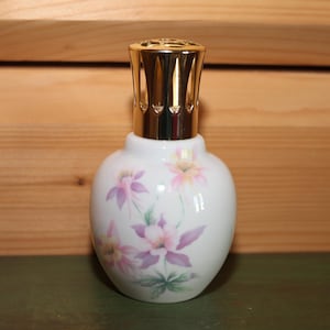 May include: White ceramic fragrance lamp with a gold-colored metal top. The lamp features a floral design in shades of pink and purple. The lamp is approximately 5 inches tall.