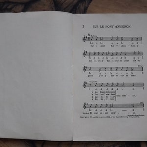 May include: A vintage music book with sheet music for the French children's song "Sur le Pont d'Avignon". The book is open to the first page, which features the lyrics and musical notation for the song.