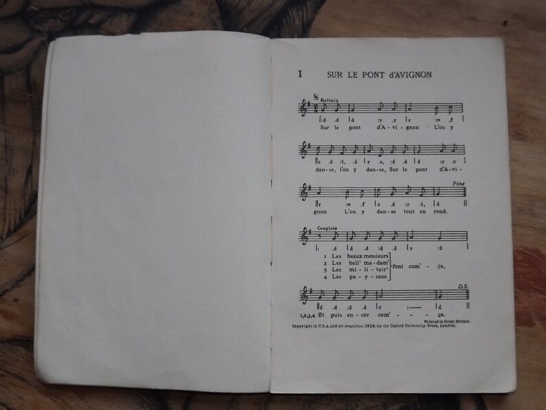 May include: A vintage music book with sheet music for the French children's song "Sur le Pont d'Avignon". The book is open to the first page, which features the lyrics and musical notation for the song.