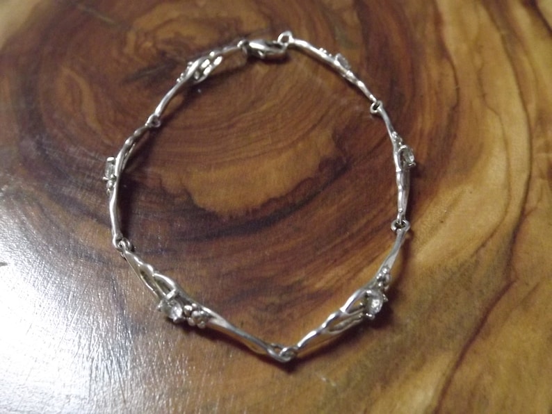 Peut inclure: Un bracelet en argent avec un design d&eacute;licat et torsad&eacute; et de petites pierres claires. Le bracelet a une fermeture &agrave; fermoir.