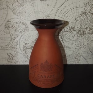 Puede incluir: Una jarra de terracota con un borde marrón y el texto "Carafe Royal Barge Ware" impreso en la parte delantera.