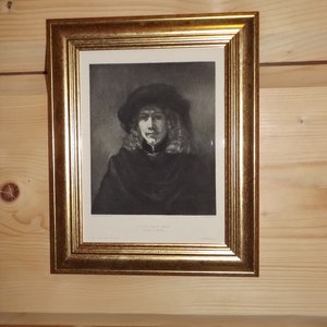 Może przedstawiać: Portret mężczyzny w czarnym kapeluszu i ciemnym płaszczu, w czarno-białej ramie. Portret nosi tytuł "Dirk van Baburen" i jest oprawiony w złotą ramę.
