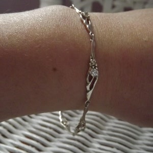 Peut inclure: Un bracelet en argent avec une cha&icirc;ne d&eacute;licate et de petites pierres claires. Le bracelet est au poignet d'une personne.