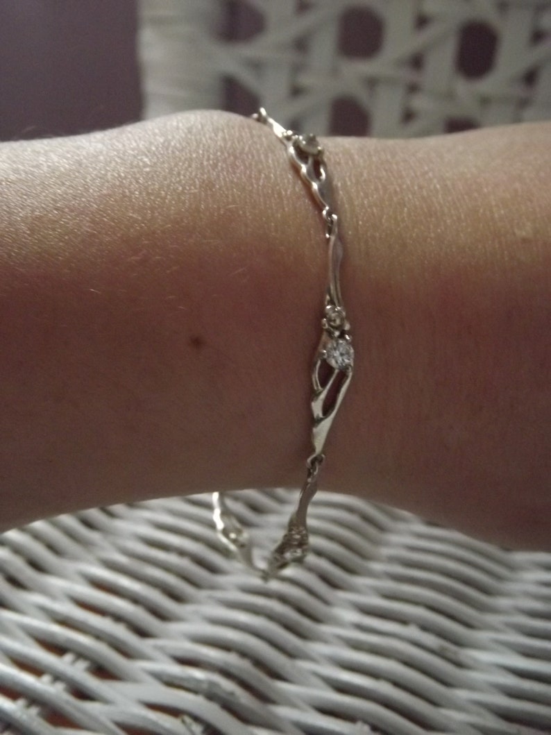 Peut inclure: Un bracelet en argent avec une cha&icirc;ne d&eacute;licate et de petites pierres claires. Le bracelet est au poignet d'une personne.