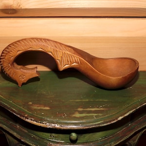 Op de afbeelding: Een houten lepel met een gesneden ontwerp, rustend op een groene houten tafel.