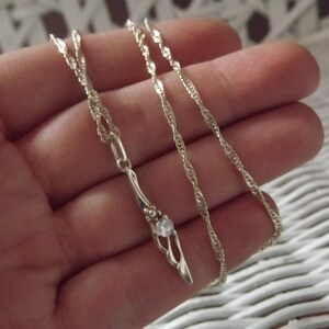 Peut inclure: Un collier en argent avec un pendentif d&eacute;licat orn&eacute; d'une seule pierre transparente.