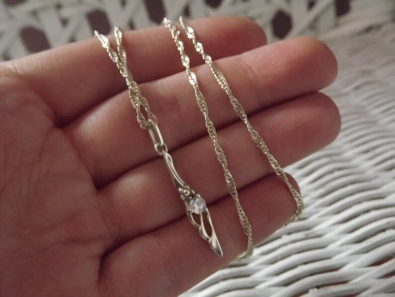 Peut inclure: Un collier en argent avec un pendentif d&eacute;licat orn&eacute; d'une seule pierre transparente.