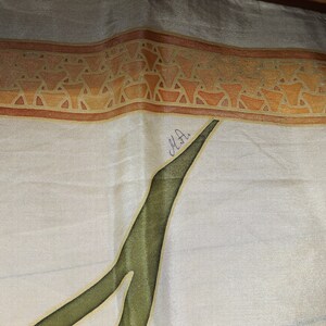 May include: A white silk scarf with a brown and orange geometric border. The scarf has a green leaf design and is signed "M.H."