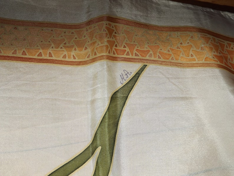 May include: A white silk scarf with a brown and orange geometric border. The scarf has a green leaf design and is signed "M.H."