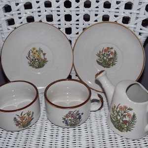 Könnte beinhalten: Ein Vintage-Blumentee-Set mit Teekanne, Tassen und Untertassen. Die Tassen und Untertassen sind weiß mit braunem Rand und einem Blumendesign. Die Teekanne hat einen braunen Griff und Ausguss.
