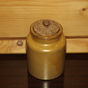 May include: A tan ceramic jar with a wooden lid and knob. The jar has a smooth, glazed finish.