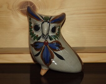May include: A ceramic owl figurine with a white base and blue, green, and brown painted details. The owl has large black eyes and a red beak.