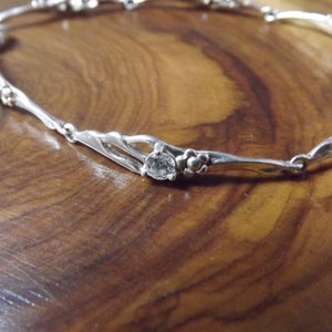 Peut inclure: Bracelet en argent avec un motif floral d&eacute;licat et des pierres claires. Le bracelet est compos&eacute; d'une fine cha&icirc;ne en argent torsad&eacute;e avec de petites fleurs.