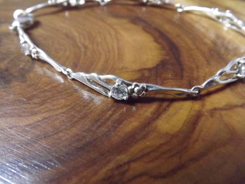 Peut inclure: Bracelet en argent avec un motif floral d&eacute;licat et des pierres claires. Le bracelet est compos&eacute; d'une fine cha&icirc;ne en argent torsad&eacute;e avec de petites fleurs.