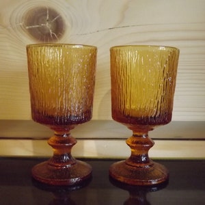 May include: Two amber-colored glass goblets with a textured, ribbed design. The goblets have a short stem and a wide base.
