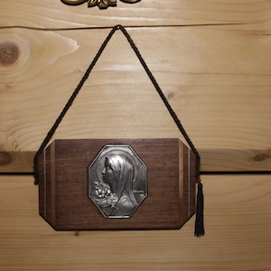 Könnte beinhalten: Eine silberfarbene religiöse Ikone einer Frau mit einem Blumendesign, gerahmt in einem dunklen Holzrahmen mit einer braunen Schnur und einem Quasten.