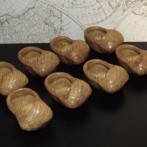 Peut inclure: Huit petits pots en céramique de couleur marron en forme de chaussure. Les pots sont disposés en rangée sur une surface noire.