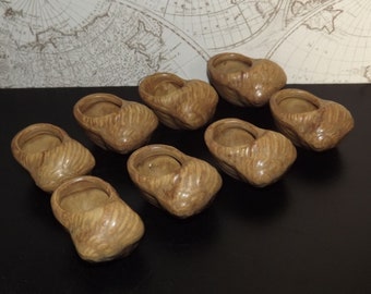 May include: Eight small, brown ceramic shoe-shaped planters. The planters are arranged in a row on a black surface.