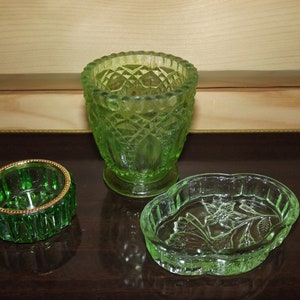 May include: Three green glass dishes with intricate patterns. The largest dish is a vase with a diamond pattern. The other two dishes are smaller and have a floral pattern.