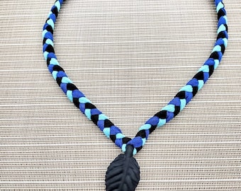 May include: A braided necklace with black, blue, and light blue cords, featuring a black leaf pendant.
