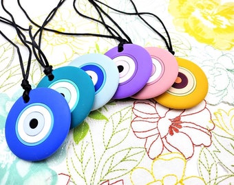 May include: Six colorful evil eye necklaces with black cords. The necklaces feature round pendants with blue, turquoise, purple, pink, and yellow evil eye designs.