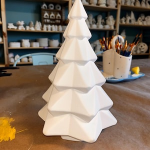 May include: White ceramic Christmas tree ornament with a geometric design. The tree is made of multiple layers of triangles that create a unique and modern look.