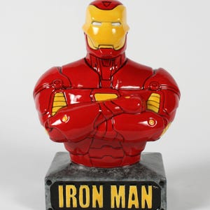 Peut inclure: Un buste de banque Iron Man en céramique. Le buste est rouge avec des détails jaunes sur le casque et la poitrine. La base est grise avec les mots "IRON MAN" en jaune. Un objet de collection.