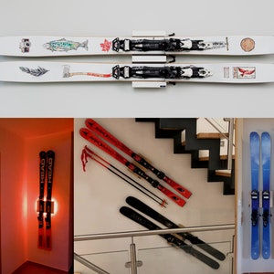 Könnte beinhalten: Mehrere Paar Ski werden an Wänden präsentiert. Ein Paar ist weiß mit schwarzen Bindungen und dekorativen Illustrationen. Weitere Bilder zeigen rote und schwarze Ski sowie blaue und gelbe Ski.