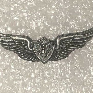 May include: A silver pilot wing with a shield in the center. The shield has a bald eagle with a banner that reads "U.S."